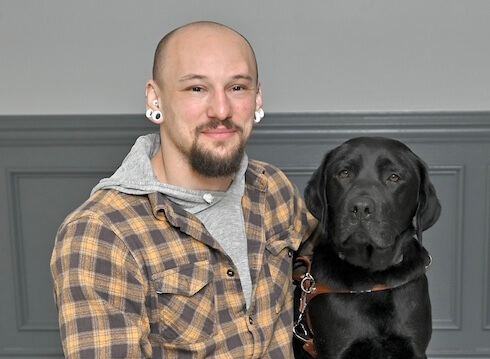 Lukas sits with black Lab guide dog Sawyer for their team portrait