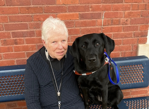 Lusi sits with black Lab guide dog Utica for their team portrait