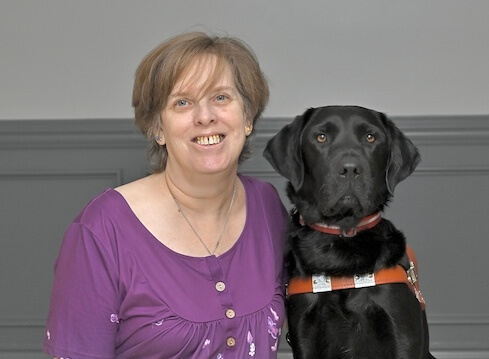 Sheila smiles sitting with black Lab guide dog Ollie for their team portrait