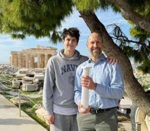 Thomas Panek holds replica of Doric column next to son Timothy against backdrop of the Parthenon in Athens.