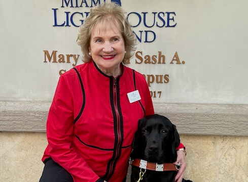 Virginia sits with black Lab guide Sama in front of a Miami Lighthouse sign
