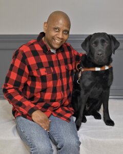 Carlton sits with arm around black Lab guide dog Laurel in their team portrait