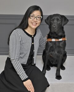 Kathryn smiles as she and black Lab guide dog Kismet sit for their team portrait