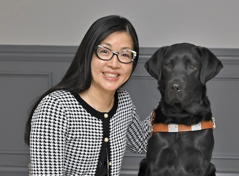 Kathryn smiles as she and black Lab guide dog Kismet sit for their team portrait