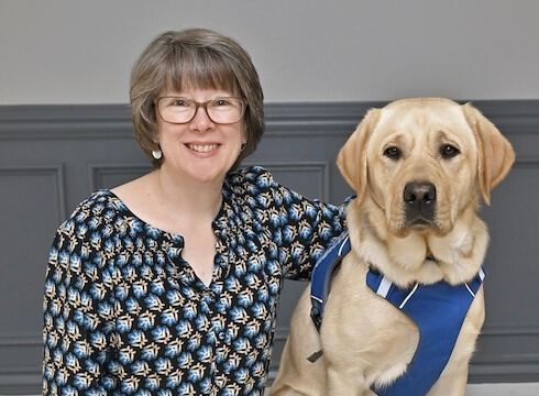 Michele sits with arm around yellow guide dog Aladdin for their team portrait