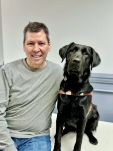 Robert smiles as he and black Lab guide dog Artemis sit for their team portrait