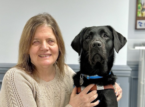 Catherine sits with hands lovingly around black Lab guide dog Jada in their team portrait