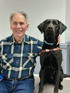 Doug sits next to black Lab guide dog Ned for their team portrait