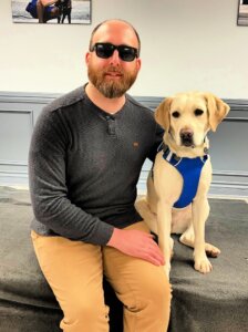 Josh and yellow Lab guide dog Moira sit for their team portrait