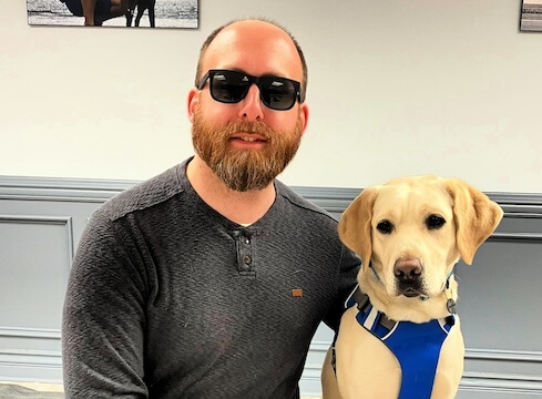 Josh and yellow Lab guide dog Moira sit for their team portrait