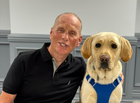 Darrell and yellow lab guide dog Klondike sit together indoors for their team portrait