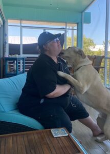 Jose sits on a cushioned chair as yellow lab guide Louis jumps affectionately to give him dog kisses