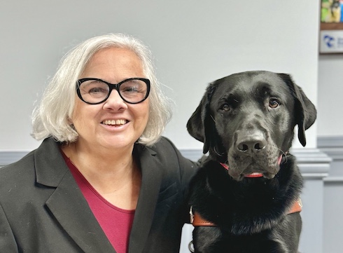 Jule Ann sits with black lab guide dog Stitch for their team portrait
