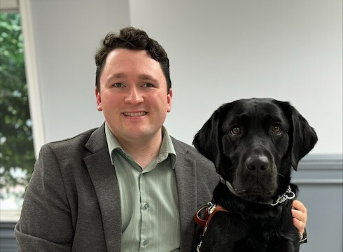 Nick and black lab guide dog Star sit together indoors for their team portrait
