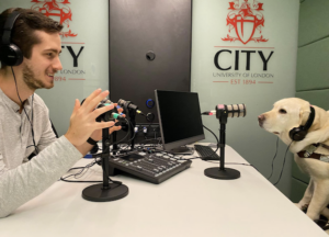 Tim sits across the table from yellow lab Alisa with audio equipment on the table and headphones on their heads