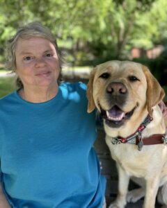 Darla and yellow lab guide dog Blaze sit together on an outdoor bench for their team portrait