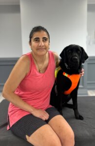 Ann and black lab guide dog Festiva sit together indoors for their team portrait