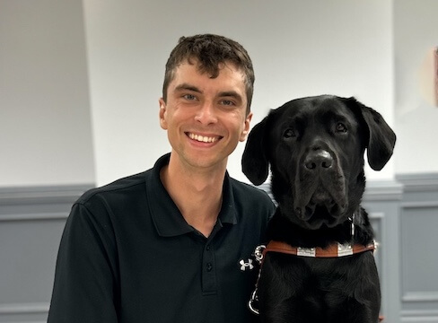 Daniel and black Lab guide dog Tank sit close with heads tilted slightly towards each other in team portrait