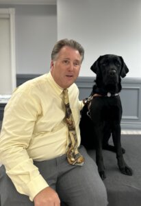 Donald and black lab guide dog Brandt sit together indoors for their team portrait