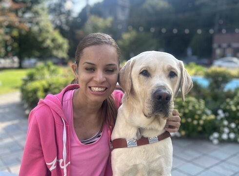 Nathalie and her yellow guide dog Olmstead, sit in a park like setting head to head for their team portrait