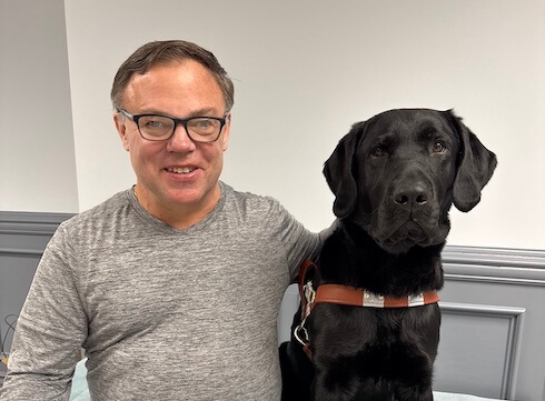 Kenneth and black Lab guide dog Dash sit side by side for their team portrait