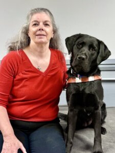 Evelyn sits with black lab guide dog Lenora for their team portrait