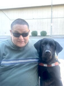 Philip and black lab guide dog Jayla sit together on an outdoor bench for team portrait