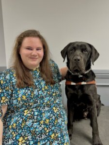 Isabelle sits side by side with her black lab guide dog Boston for their team portrait