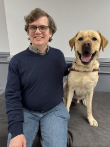 Andrew and yellow Lab guide dog Harvey sit side by side for their indoor team portrait