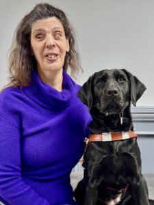 Melissa sits side by side with her black lab guide dog Ariana for their team portrait