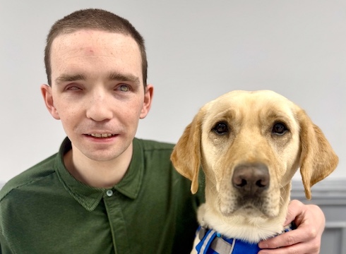 Michael and yellow Lab guide dog Yolanda sit side by side for their indoor team portrait