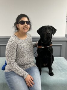 Henna and black Lab guide dog Enid sit side by side for their indoor team portrait
