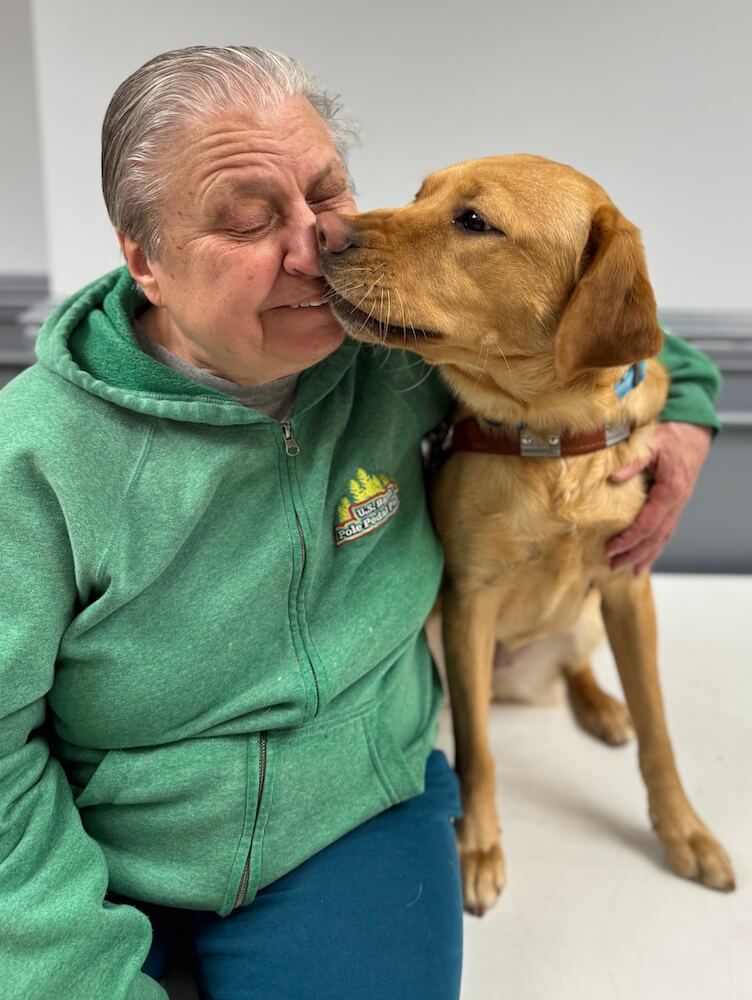Guide dog Hollywood shows some love during  team portrait photoshoot by touching her nose to Sharlene's