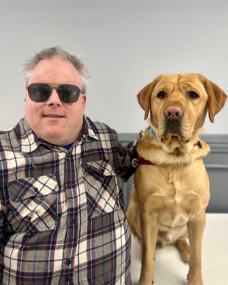 William and yellow Lab guide dog Hopkins sit side by side for their indoor team portrait