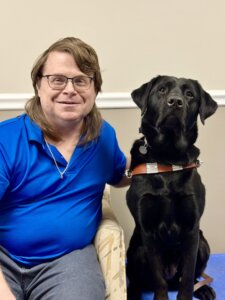 Anthony and black Lab guide dog Emily sit side by side for their indoor team portrait