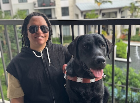 Darien and black Lab guide dog Abraham sit on the balcony of an apartment building for their team portrait