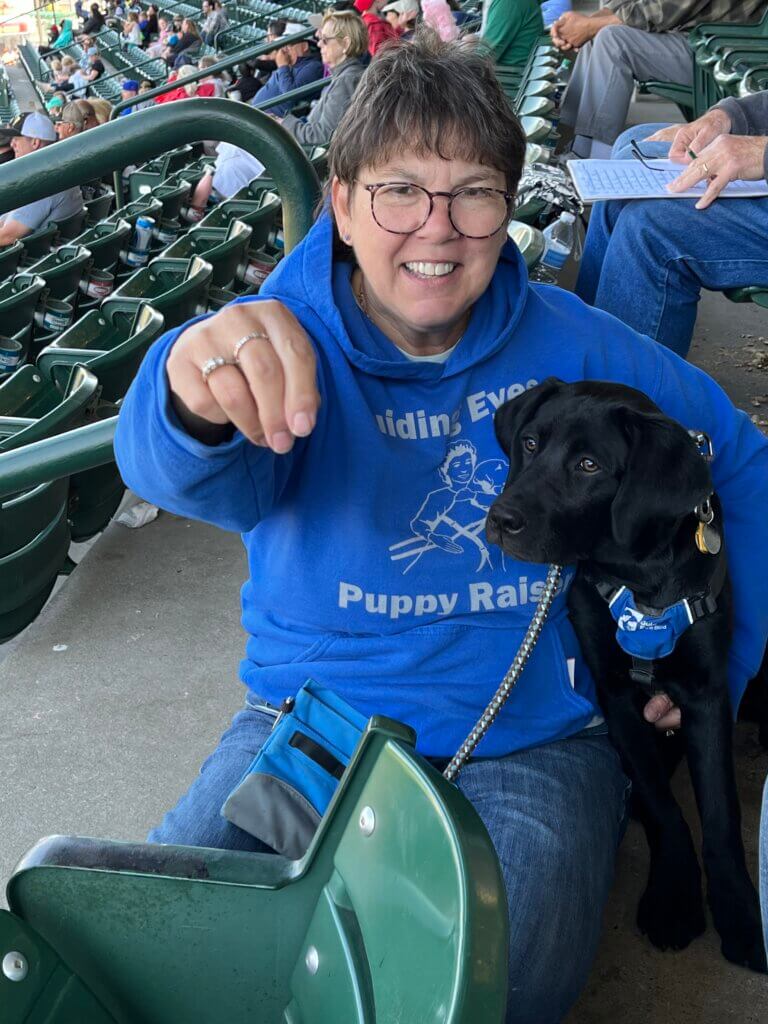 At a stadium young puppy Emily in Future Guide jacket is held by raiser