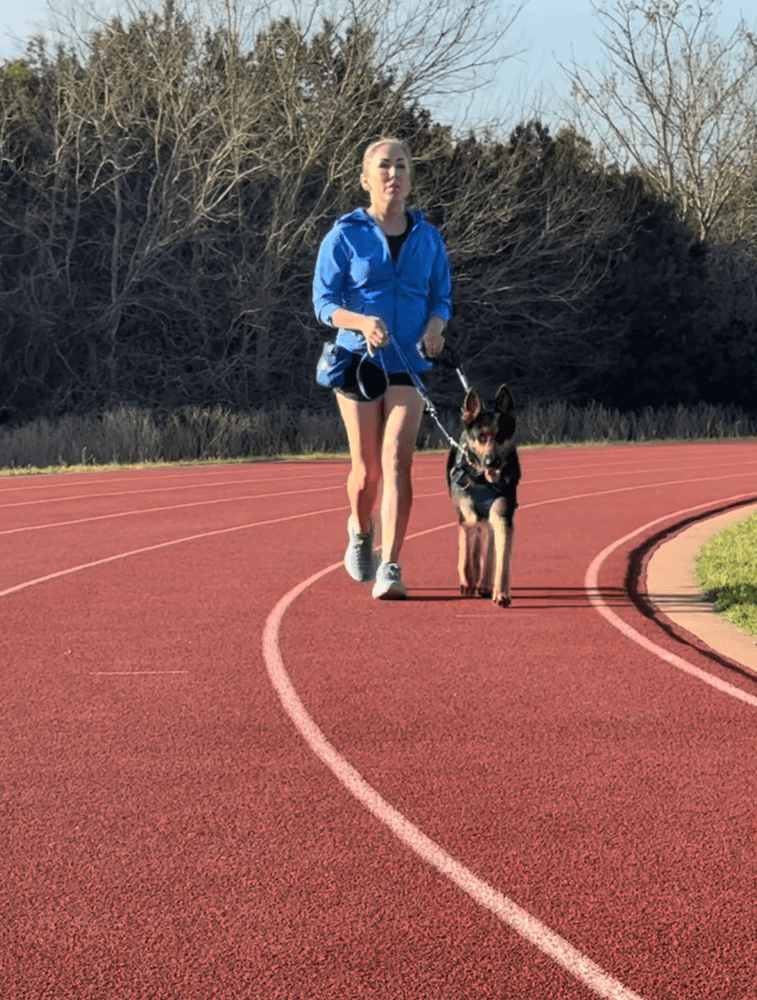 Irma runs around a red running track with German Shepherd running guide dog Wonder