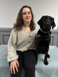 Hannah and black Lab guide dog Fate sit side by side for their indoor team portrait