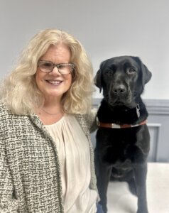 Patti sits beside her black Lab guide dog Isley for their team portrait