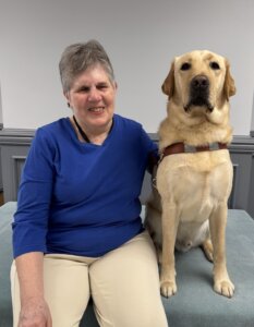 Sharon and yellow Lab guide dog Billy sit side by side for their indoor team portrait