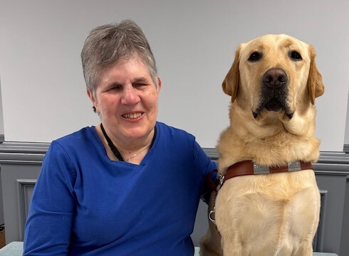 Sharon and yellow Lab guide dog Billy sit side by side for their indoor team portrait