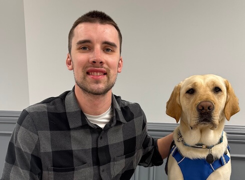 Alex and his yellow Lab guide dog Marina sit together for their team portrait