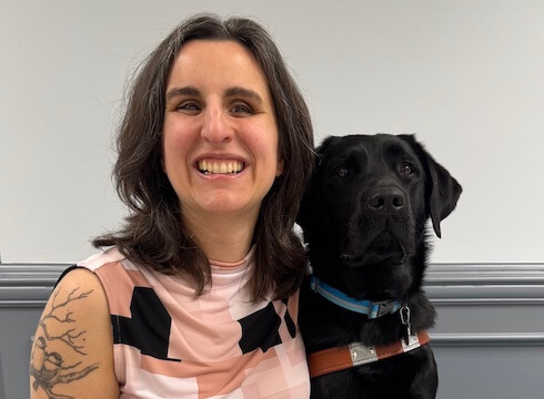 Courtney and black Lab guide dog Pinky sit side by side for their team portrait