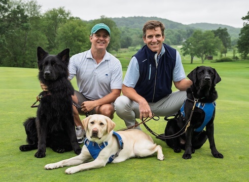 Eli Manning, board member of our organization, and Pat Browne III, on the golf course with guide dogs Angel, a black-coated Shepherd, Lavender, a yellow Lab, and Jett, a black Lab.