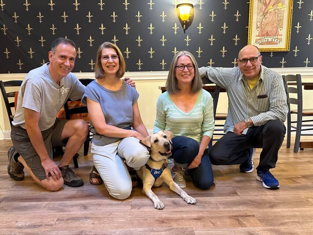 Yellow Lab pup Khaki lies on the floor in between raisers Diane and Dawn and their spouses.