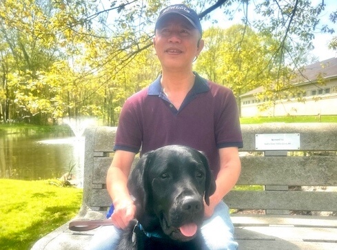 Allen and black guide dog Rex are on a park bench on the Yorktown campus for their team portrait