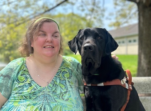 Kate and black guide dog Eagle are on a park bench on the Yorktown campus for their team portrait