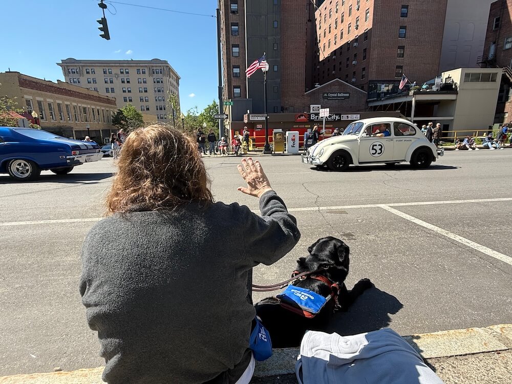 Rose waves as she and Vintage watch a vintage car parade pass by