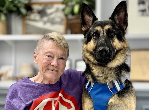 Deirdre and German Shepherd guide dog Booker sit side by side, indoors, for their team portrait